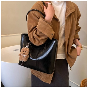Detail of black leather tote bag with a cute brown teddy bear charm and soft glossy finish