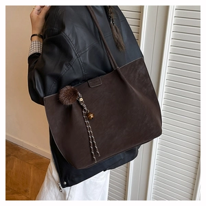 Detail of dark brown tote bag in matte suede with decorative fur ball and bell charm