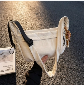 Detail of off-white nylon dumpling bag with adjustable strap and wooden bead tassel