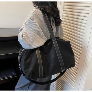 Close-up of black canvas travel tote featuring contrast stitching on leather straps