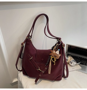 Detail view of burgundy leather shoulder bag with gold hardware and bear charm