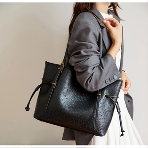 Detail of black ostrich embossed tote bag with gold hardware worn on a shoulder