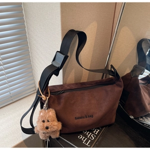 Detail of dark brown suede crescent bag with adjustable strap and bear charm