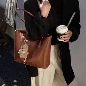 Brown leather tote bag with a cute bear charm and long straps for daily commuting