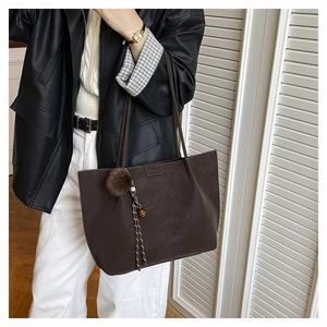 Brown large capacity tote bag with tassel charm detail shown on a female model