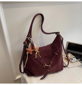 Detail of burgundy hobo bag with star and bear charms on white desk surface
