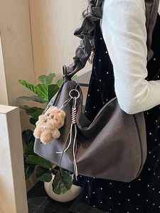 Brown oversized tote bag with scrunchie strap and plush charm worn by a model