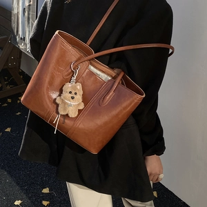 Brown faux leather tote bag with plush bear charm worn on shoulder with black coat