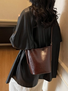 Vintage dark brown bucket bag with glossy leather finish worn over the shoulder
