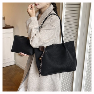 Detail of black tote bag set with brown pompom and textured matte finish on a model