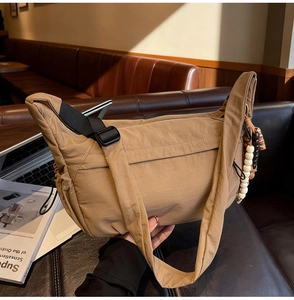 Detail of khaki nylon crossbody bag with wooden bead charm on a leather sofa
