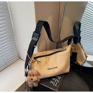 Detail of beige suede crossbody bag with wide black strap and brown teddy charm