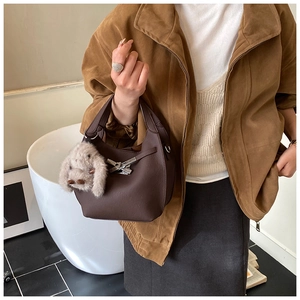 Detail of dark brown lychee leather bucket bag with metal buckle and plush bunny charm