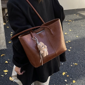 Brown vintage faux leather tote bag with a cute bear charm shown in an autumn setting