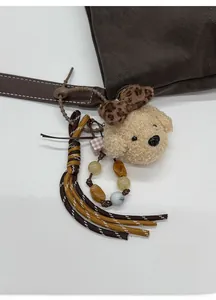 Detail of plush dog pendant with leopard bow and beaded ring on brown tote bag
