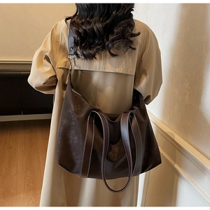 Detail of large dark brown tote bag on model showing soft texture and contrast stitching