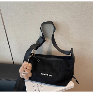 Detail of black suede dumpling bag with adjustable strap and cute teddy dog keychain