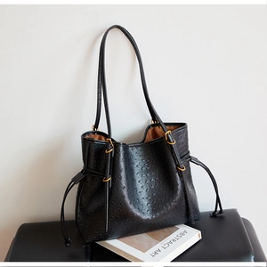 Close-up of black ostrich texture tote bag with drawstring closure and golden buckle