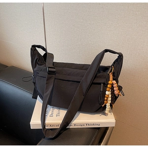 Detail of black nylon crossbody bag with adjustable strap and ethnic beaded charm decoration