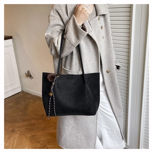 Detail of black matte leather tote bag with plush charm on light grey coat outfit