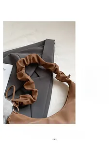 Detail of a brown crescent shoulder bag featuring a pleated strap and a white fur charm