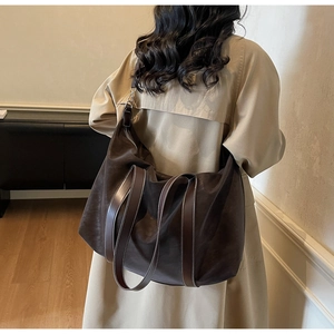 Detail of dark brown matte tote bag with contrast stitching on glossy leather handles