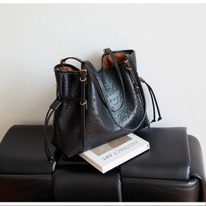 Detail of black ostrich embossed leather tote bag featuring gold hardware and drawstrings