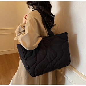 Close-up of quilted wave pattern on black tote bag with shoulder strap detail