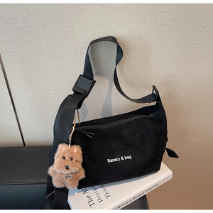 Detail of black suede dumpling bag with brand logo and brown plush puppy charm
