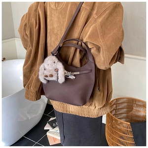 Detail of crescent shoulder bag in dark brown with metal lock and plush bunny charm