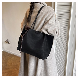 Close-up of black matte tote bag featuring pom-pom charm and woven rope detail