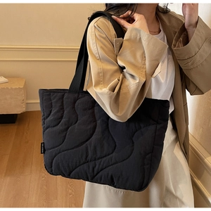 Detailed wave quilted texture on a large black puffer tote bag with a brand side label