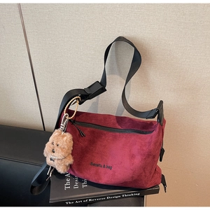Detail of burgundy suede crossbody bag with embroidery and cute teddy bear charm