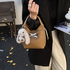 Detail of tan pebble leather bucket bag with silver bow buckle and plush rabbit charm