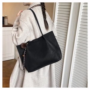 Detail of large black leather tote bag with pompom and ribbon hanging from shoulder