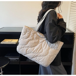 Detail of the wave quilted texture and side label on a large beige puffer tote bag