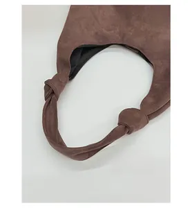 Close-up of wide knotted shoulder strap on brown suede tote bag with black lining