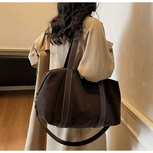 Large brown suede travel bag shown over the shoulder of a model in a trench coat
