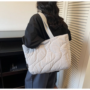 Detail of light grey quilted tote bag with wavy stitching and brand label on shoulder