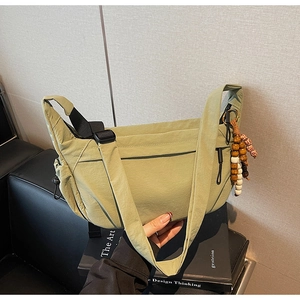 Light green nylon shoulder bag featuring wide strap and colorful beaded charm detail