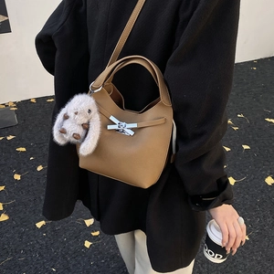 Detail of tan leather bucket bag featuring a silver bow buckle and plush rabbit charm