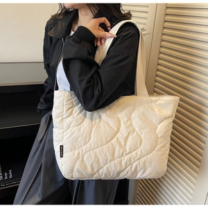 Detail view of cream quilted tote bag showing wavy stitching and fabric shoulder strap