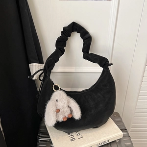 Detail of black hobo bag with ruffled shoulder strap and plush rabbit charm accessory