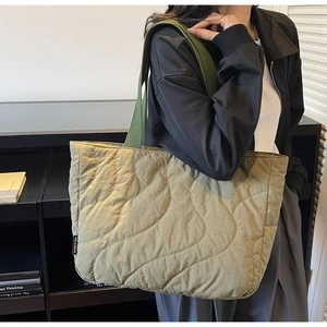 Detailed side view of an olive green quilted tote bag featuring an embroidered brand label