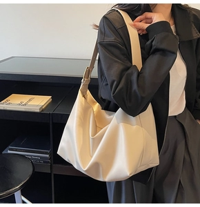 Close-up of a cream leather tote bag with a golden adjustable buckle and wide strap