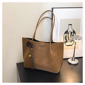 Close-up of brown suede tote bag with decorative tassel charms and branded logo detail
