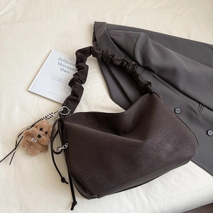 Detail of coffee brown pleated shoulder bag with scrunchie strap and plush dog charm