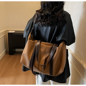 Detail of a large brown faux leather tote bag with dual straps worn by a model