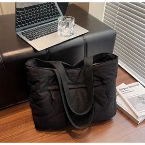 Close-up of black quilted tote bag with wave stitching and decorative front zipper pocket