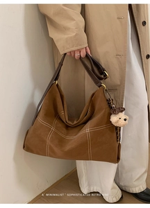 Detail of vintage matte leather tote bag with white cross-stitching and plush bear charm